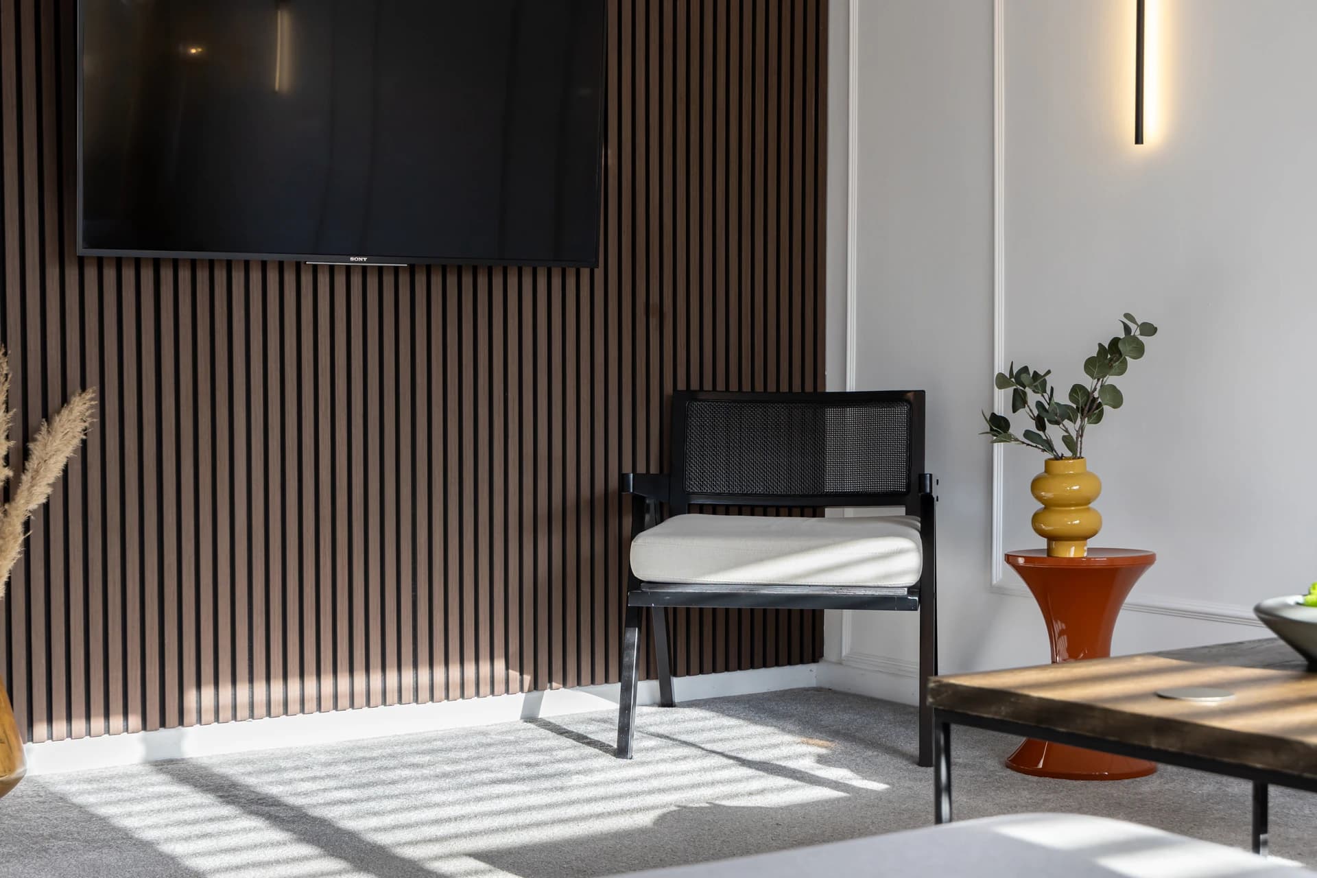 Wood-slat feature wall with TV and accent chair in the living room at Amberwood Drive