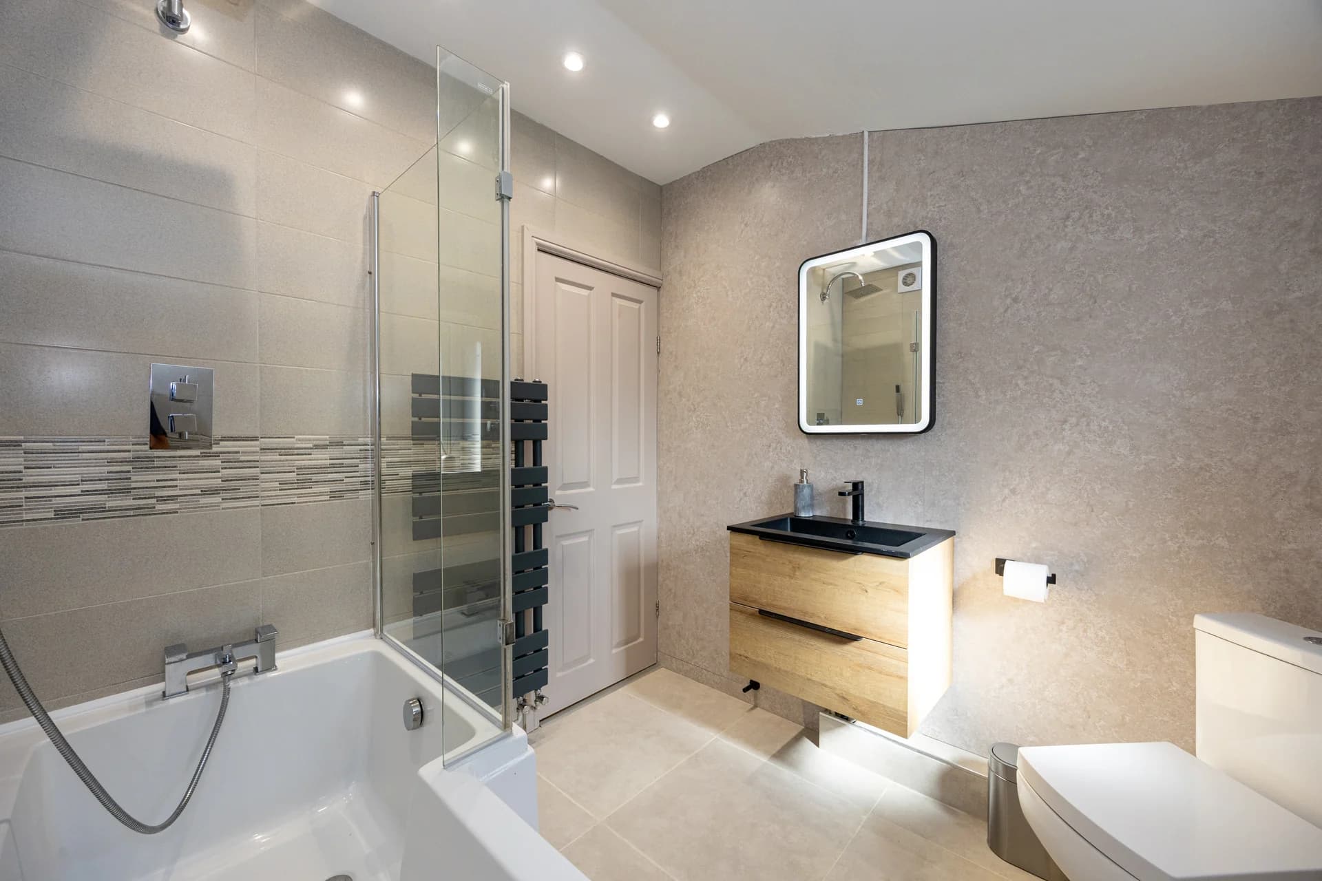Bathroom with bath, shower screen and lit mirror at Meadow Croft, Wythenshawe
